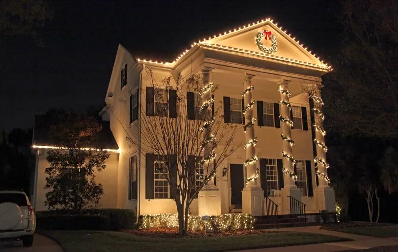 Two-story white colonial in Portland with warm white C9 lights along every roofline and lit wreaths on the columns